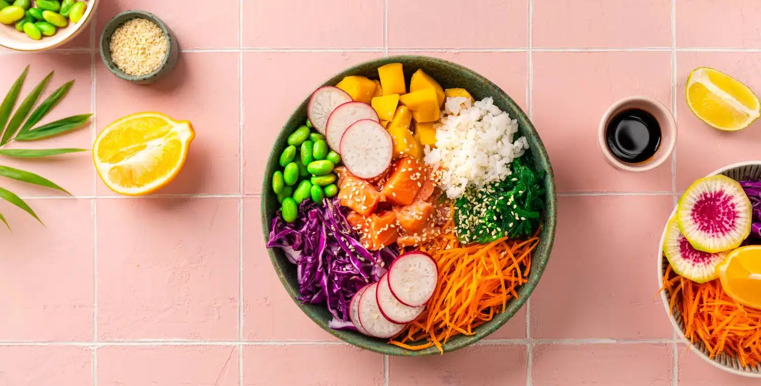 Colorato bowl di poke con riso, salmone, edamame, pomodori, mango e verdure fresche, ideale per un pasto salutare e gustoso, con limone e salsa di soia.