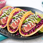 Tacos di tonno piccante con salsa mayo al lime, serviti in tortillas croccanti con verdure fresche e cavolo rosso, perfetti per un piatto di pesce gustoso e originale.
